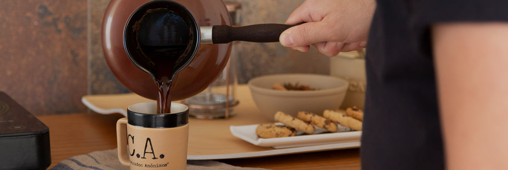 Imagem ambientada com uma pessoa servindo-se de café, mesa posta com louças e biscoitos.