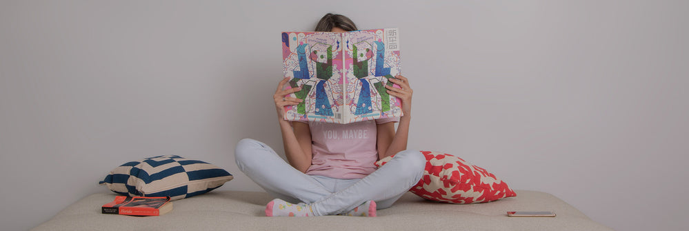 Imagem apresentando uma pessoa lendo em um ambiente aconchegante com livros, tapete e almofadas.