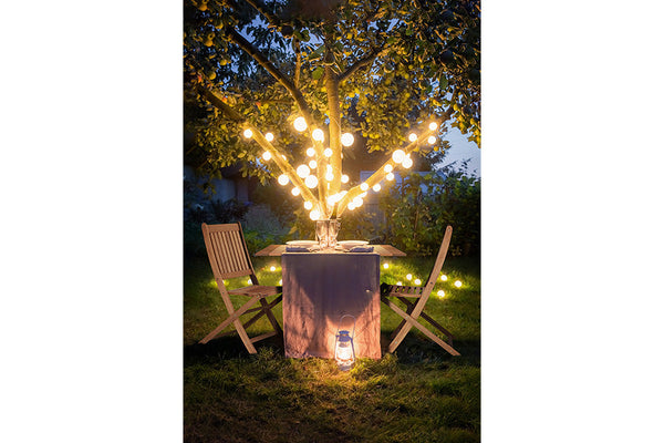cadeira madeira dobravel jatoba em jardim com mesa dobravel e arvore com luzes ao fundo