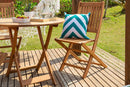 cadeira para varanda dobravel jatoba vista na diagonal com almofada sobre ela mesa dobravel ao lado e grama ao fundo
