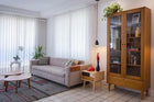 foto ambientada da cristaleira madeira retro charme doce de leite escovado vista pela lateral com objetos dentro com mesa lateral e sofa ao lado
