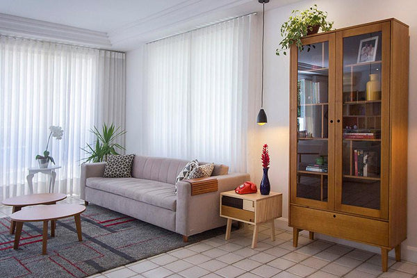 foto ambientada da cristaleira madeira retro charme doce de leite escovado vista pela lateral com objetos dentro com mesa lateral e sofa ao lado