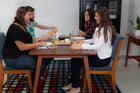 foto ambientada da mesa 6 lugares lotus caramelo vista de lado com 4 cadeiras com pessoas sentadas e loucas sobre o tampo