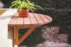 foto ambientada da mesa pequena de madeira dobrável legno jatobá vista pela lateral fixada na parede com planta sobre ela em área externa