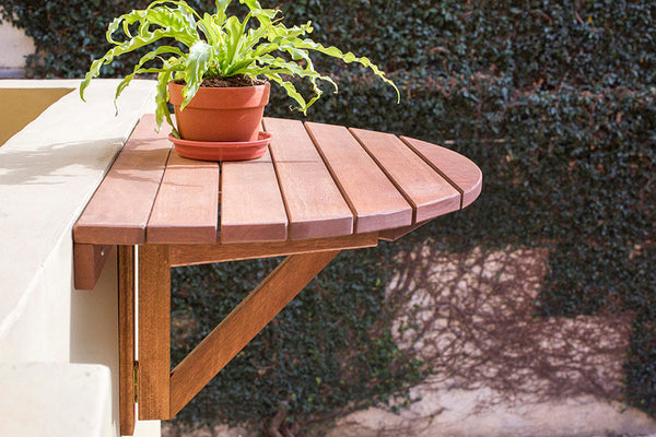 foto ambientada da mesa pequena de madeira dobrável legno jatobá vista pela lateral fixada na parede com planta sobre ela em área externa